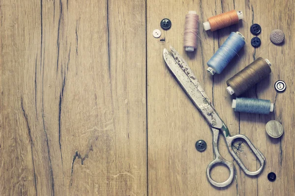 Sewing kit. Scissors, bobbins with thread and needles on the old wooden background