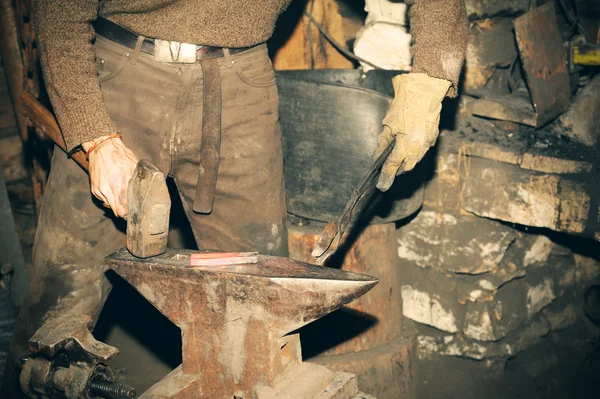 Blacksmith working in the forge processes the metal .