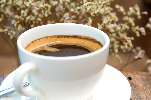 White coffee cup with dry flower on wooden table.