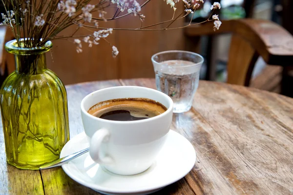 White coffee cup with dry flower on wooden table.