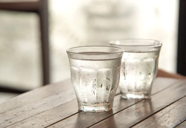 Glass water on wooden table with poor light background.