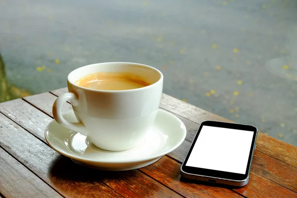 White coffee cup with smart phone on wooden table.