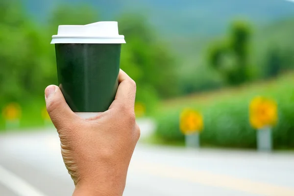 Green take away coffee cup in man hand with blurred road backgro