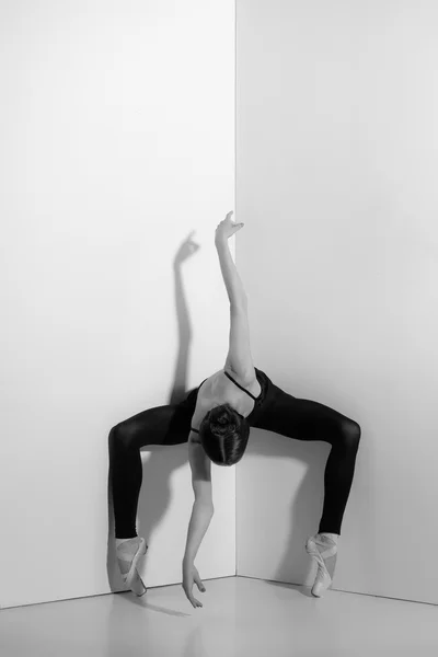 Ballerina in black outfit posing on pointe shoes, studio background.