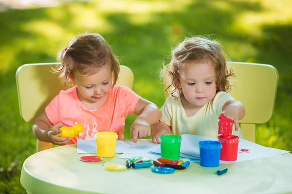 Two-year old girls painting with poster paintings together against green lawn