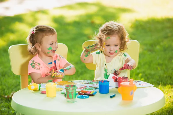Two-year old girls painting with poster paintings together against green lawn
