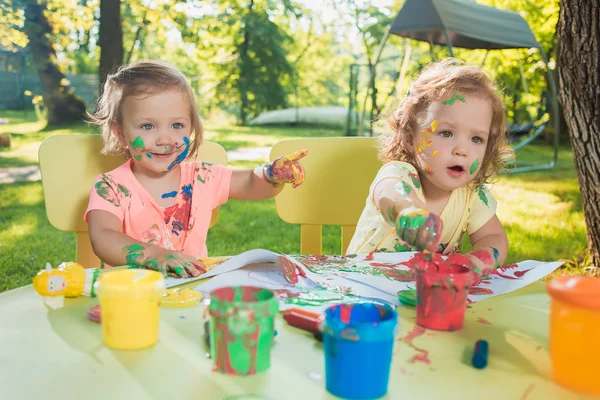 Two-year old girls painting with poster paintings together against green lawn