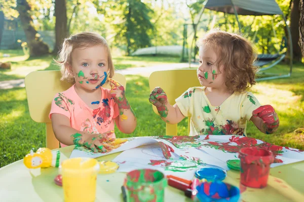 Two-year old girls painting with poster paintings together against green lawn