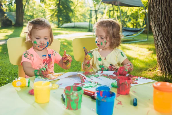 Two-year old girls painting with poster paintings together against green lawn