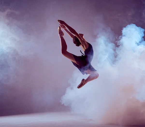 Beautiful young ballet dancer jumping on a lilac background.