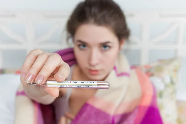 Young sick woman in blanket with thermometer