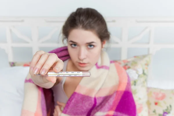 Young sick woman in blanket with thermometer