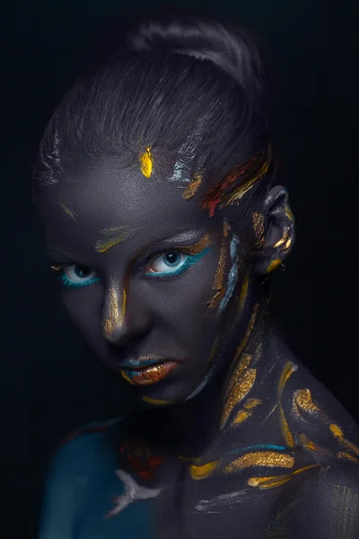 Portrait of a young woman who is posing covered with  black paint