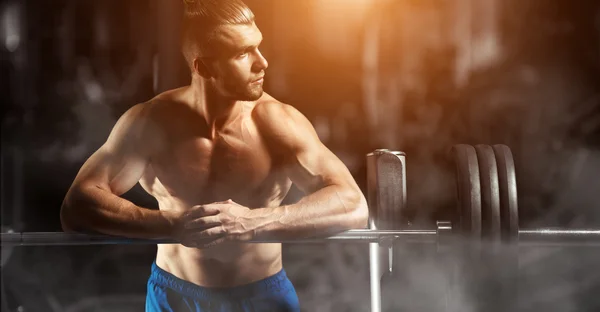 Attractive muscular bodybuilder guy prepare to do exercises with barbell in a gym