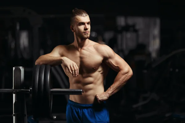 Attractive muscular bodybuilder guy prepare to do exercises with barbell in a gym