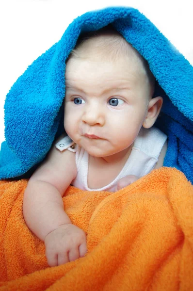 Two and half month adorable baby , looking out under a blue and orange blanket or towel