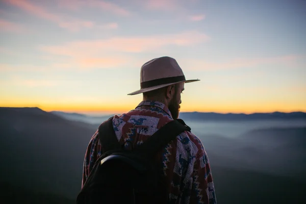 Man with hat and bag looking at the sunset