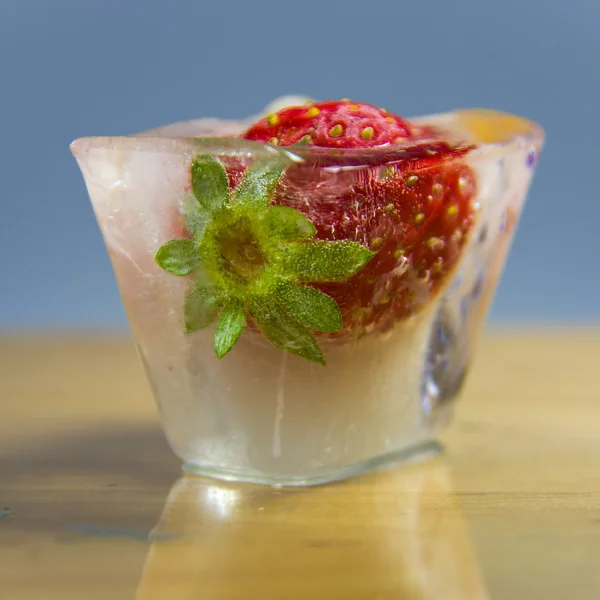 Frozen strawberries in a block of ice on a wooden surface