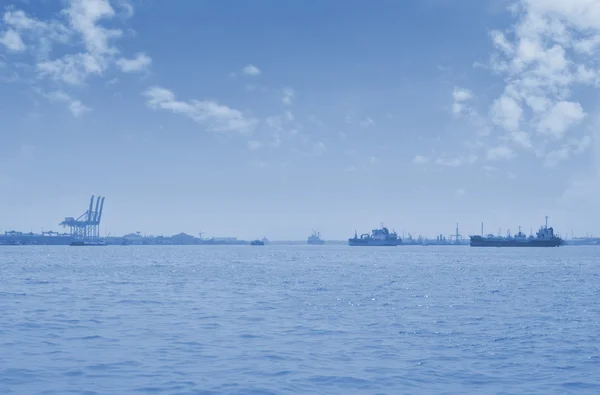 Cargo ship with shipping port over sea and sky, blue tone