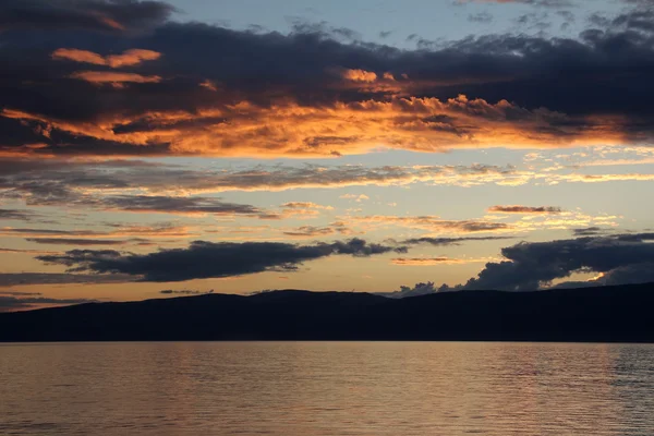 Beautiful sunset with orange-yellow sky with clouds at the lake, river. Nature of Baikal lake, Olkhon Island, Russia