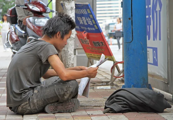 Guy in the dirty clothes is reading newspaper on street in Kunming
