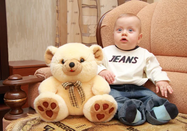 Baby with big blue eyes sit next to teddy bear