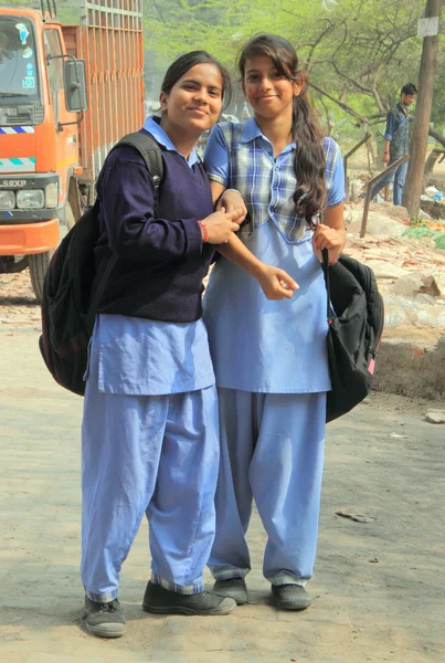 Two girls in school clothes are smiling to someone