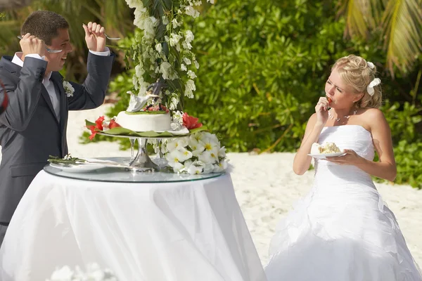 Lovely couple eating wedding cake during tropical marriage cerem