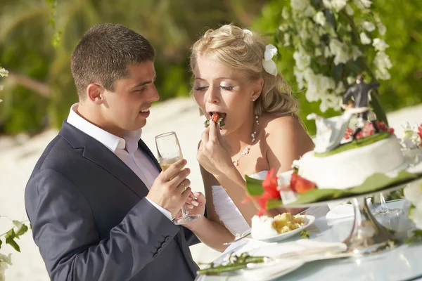 Lovely couple eating wedding cake during tropical marriage cerem