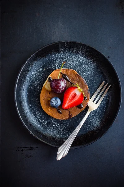 Pancake with fresh berries and chocolate sauce on  black plate