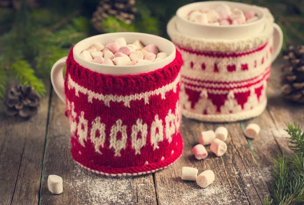 Mugs with hot chocolate and murshmallow, wrapped in a winter kni