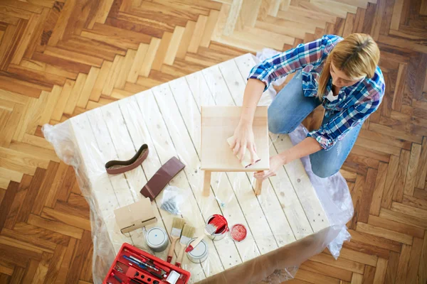 Young woman sanding furniture at home