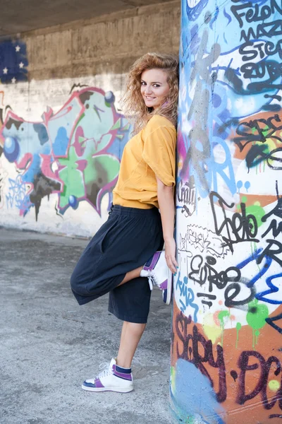 Happy hip teenage blonde girl standing by graffiti wall