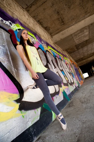 Teenage girl with gray hat dancing in front of graffiti wall