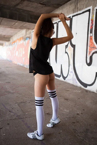 Beautiful woman with black sunglasses and black sport clothing sexy dancing in front of graffiti wall