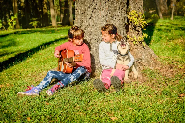 Little girl playing guitar in the park with husky puppy singing
