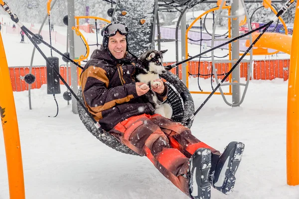 Man  sitting on the swing with husky puppy dog in the winter tim