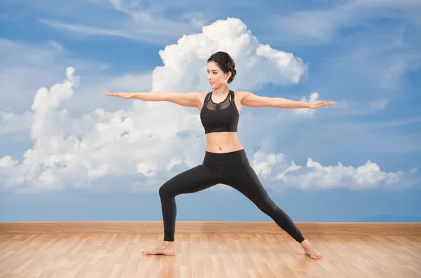 Young woman practicing yoga on wooden floor with blue sky background