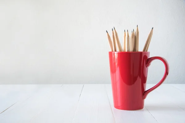 Pencils in red cup on white wooden table