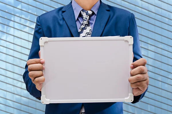 Business man holding white board with modern building background