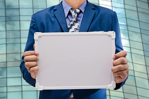 Business man holding white board with modern building background