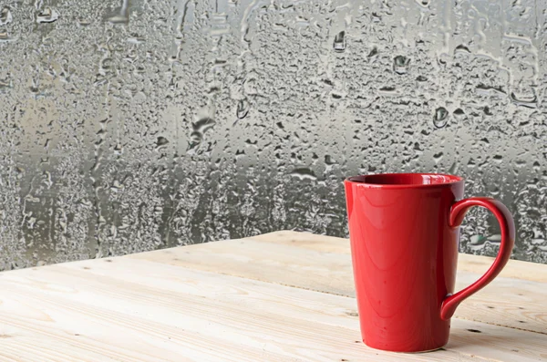 Red coffee cup with natural water drops on glass window backgrou