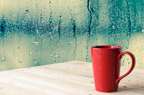 Red coffee cup with natural water drops on glass window backgrou