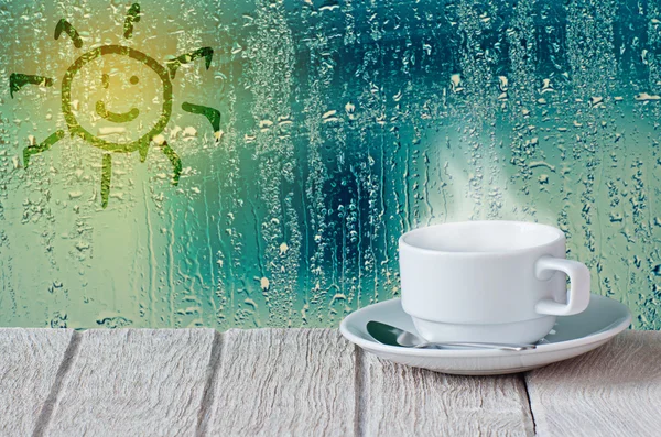 Coffee cup with water drops on glass window and sun symbol backg