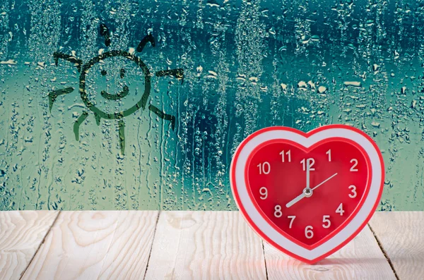 Red clock on rain drop and sun sign glass window background