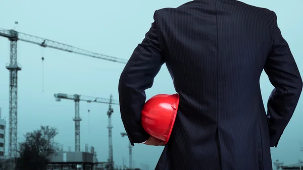 Business man holding red safety helmet with construction site ba