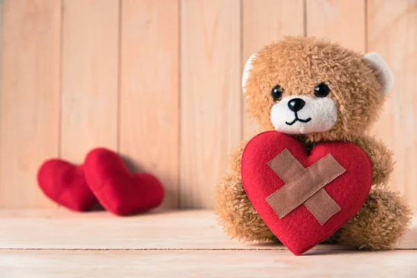 Teddy bear holding wound heart with couple red heart background