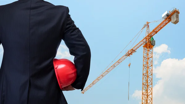 Business man holding red safety helmet with construction site ba