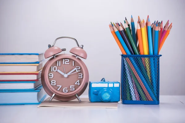 Color pencil box , alarm clock and stack of book on wooden table