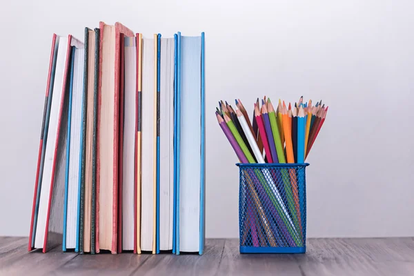 Color pencil box and stack of book on wooden table